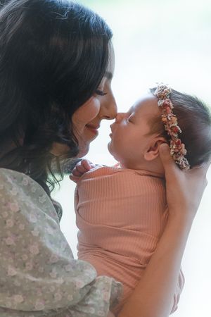 An intimate close-up portrait showing a tender nose-to-nose moment with a baby in pink.