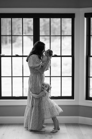 Silhouettes by a bay window show a gentle family moment with flowing dresses and natural light in the Hudson Valley,NY.