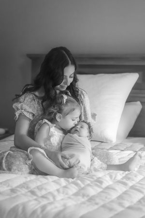A black and white photograph capturing a quiet moment between family members on a bed.