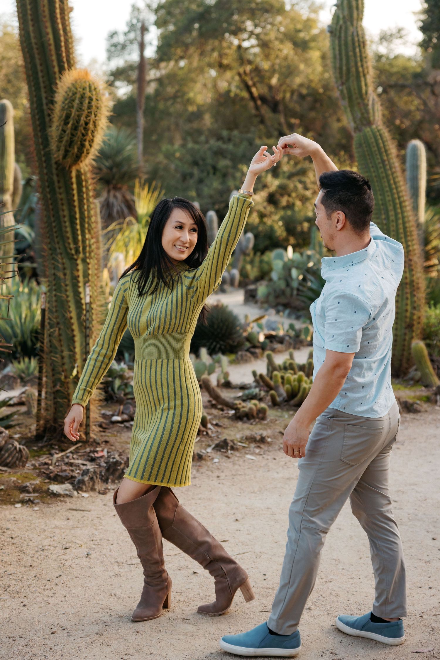 Couple dances playfully on path surrounded by tall desert cactus plants.