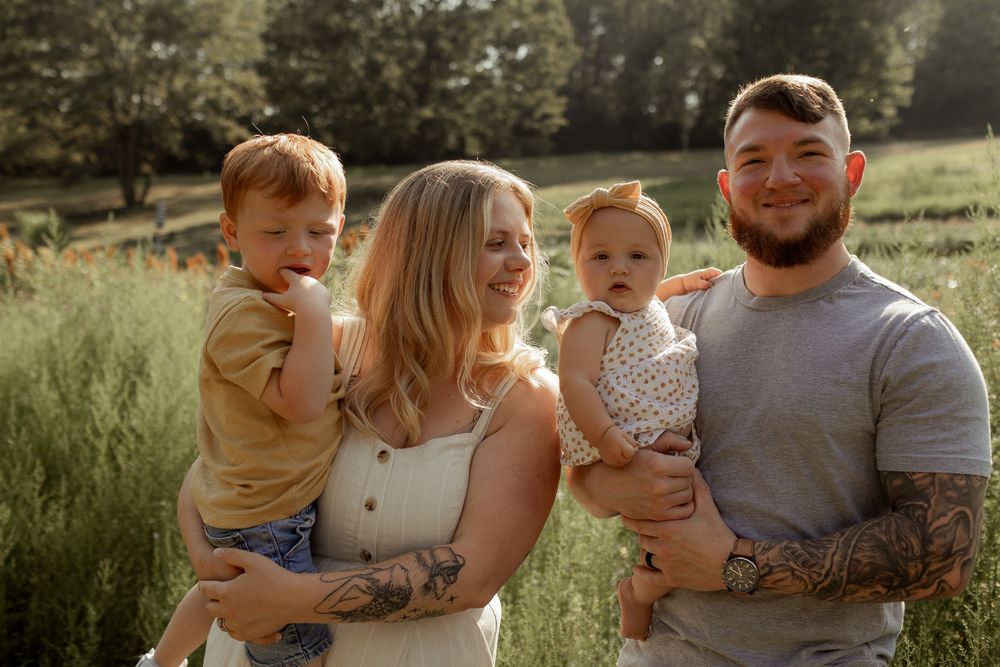 A happy family of four poses together in a sunlit meadow during golden hour.