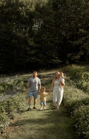 A family walks together on a sunlit nature trail surrounded by lush greenery and wildflowers on a summer day.
