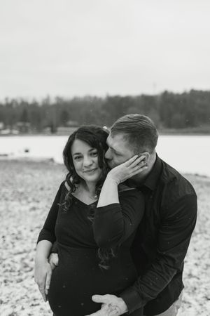 A couple shares intimate candid moments in a series of black and white photos on a snowy beach.