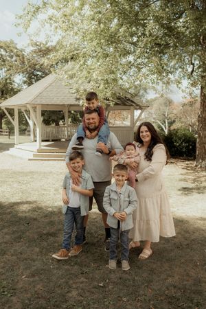 A family shares joyful moments together outdoors on a sunny day beneath shady trees.