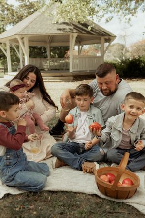 A family enjoys a picnic on a blanket outdoors with apples and snacks on a sunny autumn day.