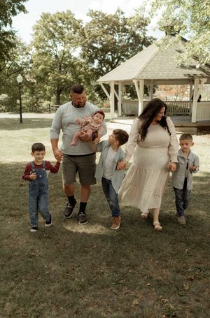 A family walking together in a line across a grassy lawn near a white gazebo on a sunny day.
