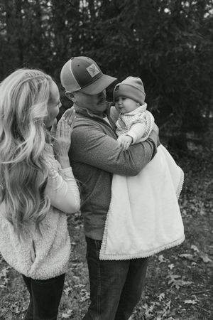 Black and white series showing an intimate family moment outdoors with fallen leaves and trees in the background.