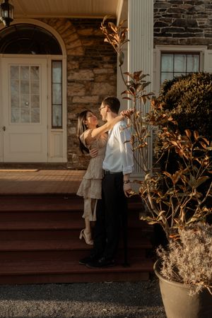 A couple shares a romantic moment on the front steps of a stone building at sunset.