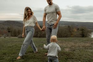 A family walks hand in hand across a hilltop meadow with sweeping autumn valley views in the background.