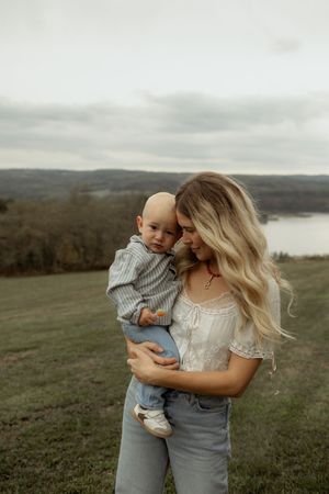 A tender moment shared between parent and child on a hilltop overlooking a serene lake on an overcast day.