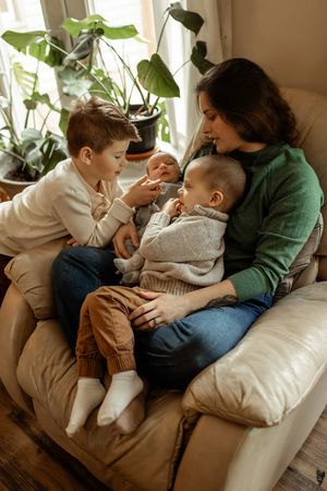 Family members share tender moments while relaxing together on a comfortable couch with houseplants in background.