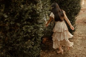 A person in a flowing beige dress walks through a sunlit forest path during golden hour.