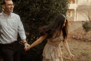 A couple holds hands and laughs together during a romantic sunset photoshoot in a rustic outdoor setting.