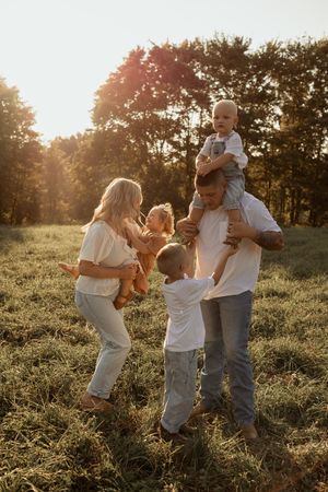 A family enjoys a golden sunset moment together in a grassy field surrounded by trees.
