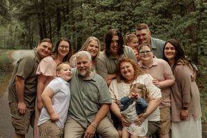 A joyful extended family poses together outdoors in a forest setting wearing coordinated neutral colored outfits.