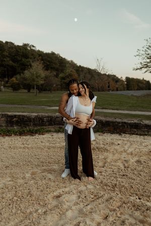 A couple embraces intimately while standing in a rustic outdoor setting at dusk.