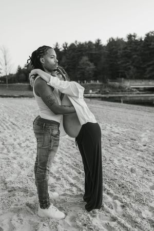 Two children playing and hugging in a sandy field with pine trees in the background.