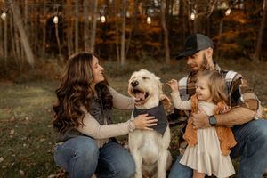 A family and their golden doodle dog pose together in an autumn forest setting during a photo session.
