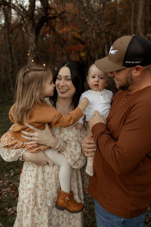 Family shares tender moments together during autumn photo session in the woods wearing brown and floral outfits.
