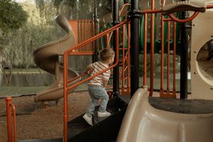 A child in a striped shirt climbs up playground equipment with a spiral slide visible in the background.