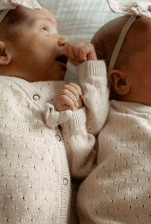 Baby wearing soft cream knit sweater lying down in tender moment against neutral background.