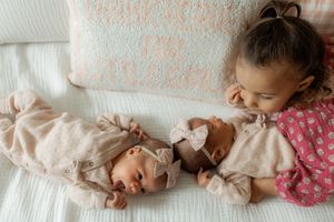 A sleeping baby lies on white bedding wearing a pink floral outfit.