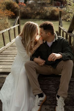 Romantic couple in casual attire share intimate moments on a rustic wooden bridge during autumn.