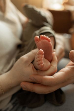 Adult hands gently cradle tiny newborn baby feet in warm, soft lighting creating an intimate nurturing moment.