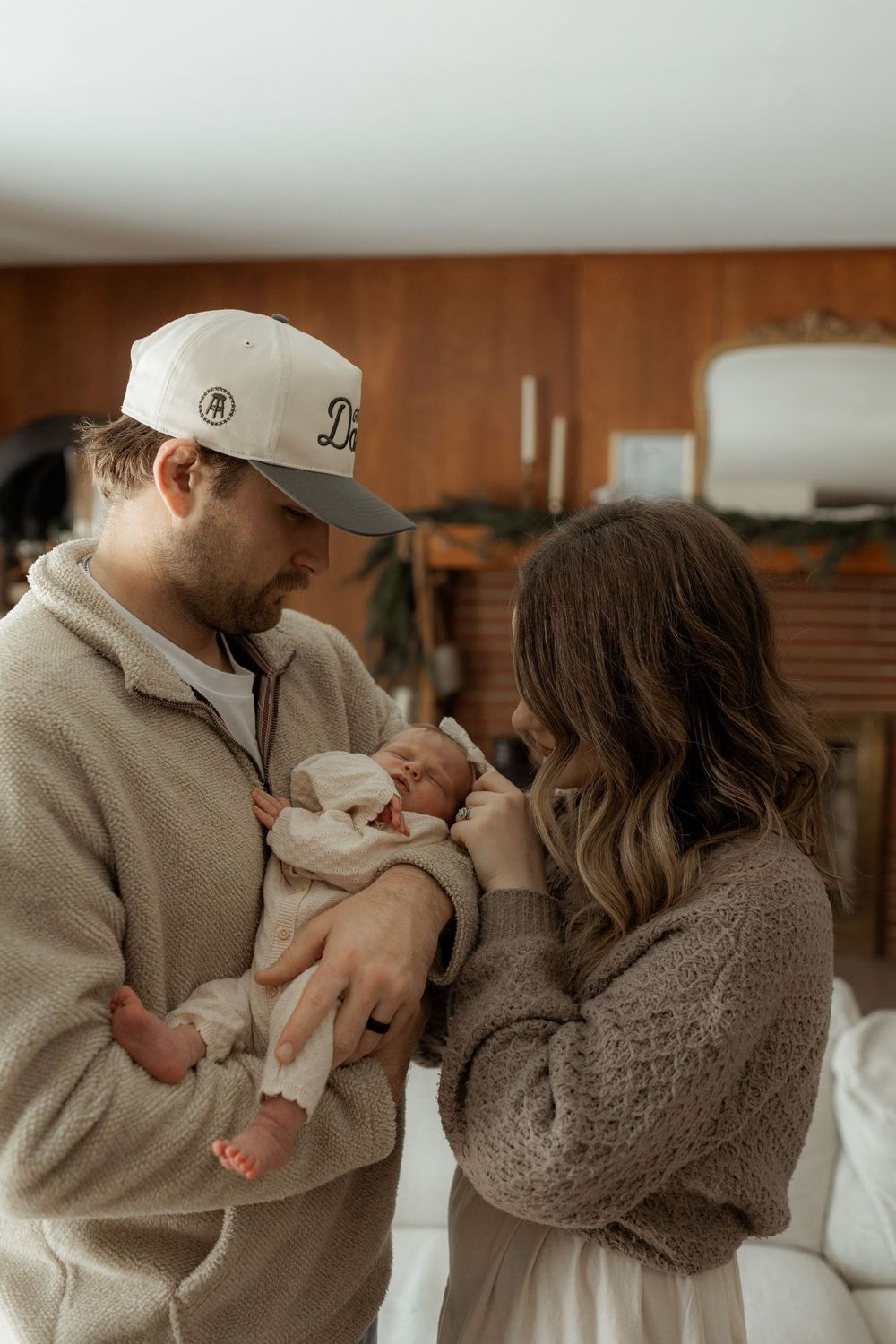 Parents in cozy sweaters tenderly hold and gaze at their newborn baby in a warm, intimate home setting.
