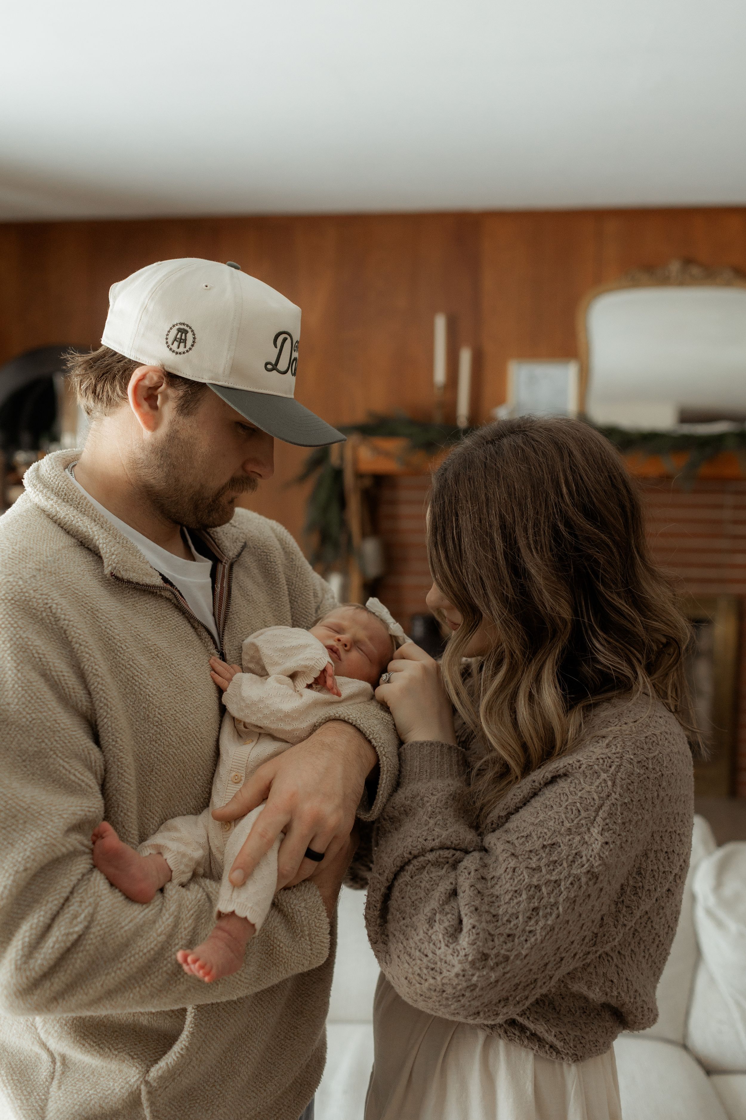 Parents in cozy sweaters tenderly hold and gaze at their newborn baby in a warm, intimate home setting.