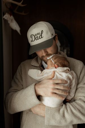 A series of photos showing someone in a beige sweater and baseball cap cradling and feeding a small baby.