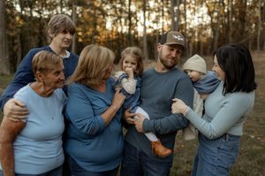 Three generations of family members gather outdoors in coordinating blue outfits during golden hour in autumn.