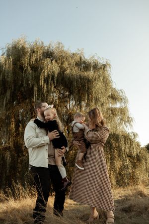 A family shares tender moments together under a large weeping willow tree on a golden afternoon.