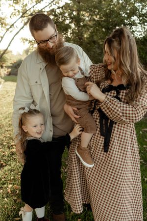 A family shares joyful moments together in a sunlit outdoor setting wearing brown and white clothing.