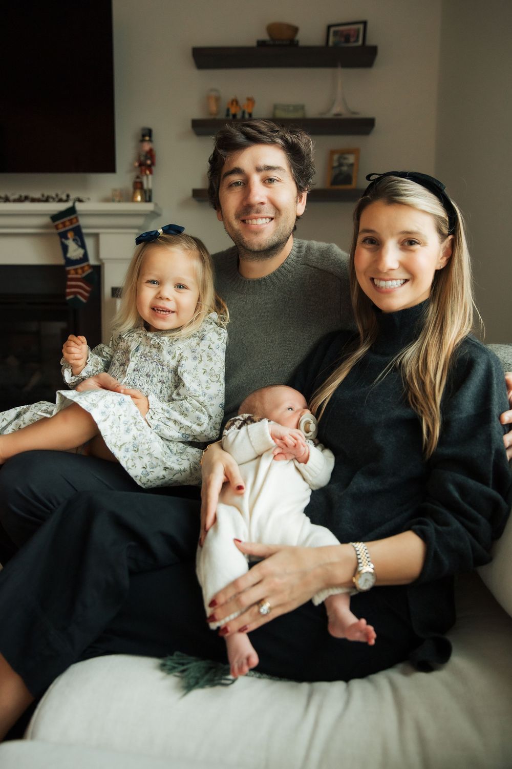 Happy young family with toddler girl and newborn baby posing together on a couch in a cozy living room. Portsmouth Rhode Island