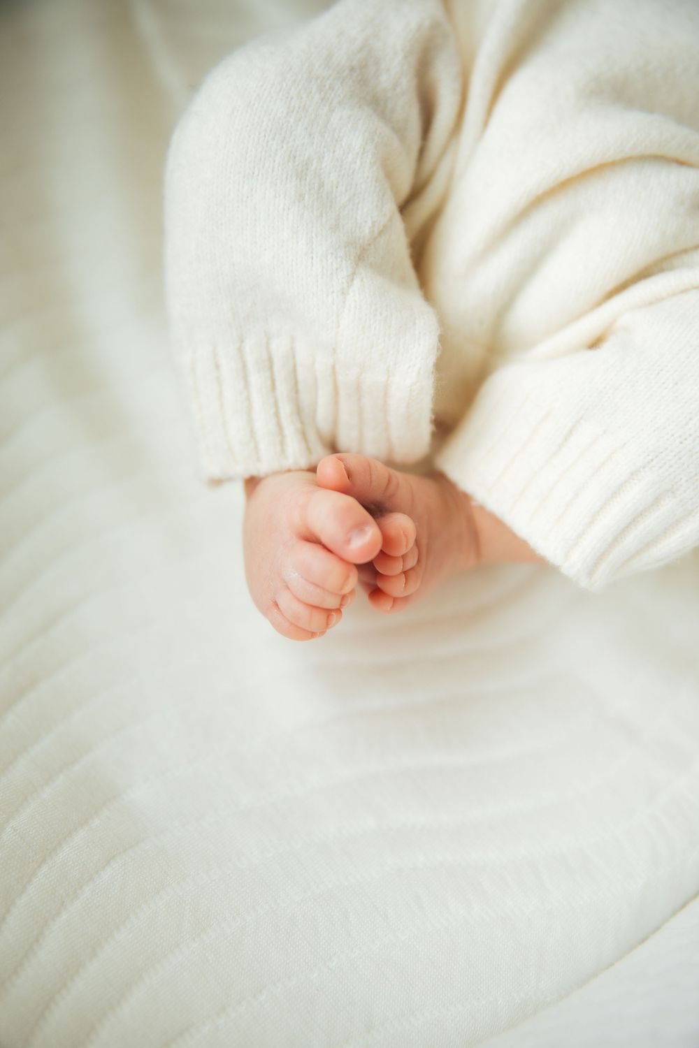 Close-up of a newborn baby's tiny toes peeking out from a soft white knit sweater sleeve on a white blanket. Bristol Rhode Island Portsmouth