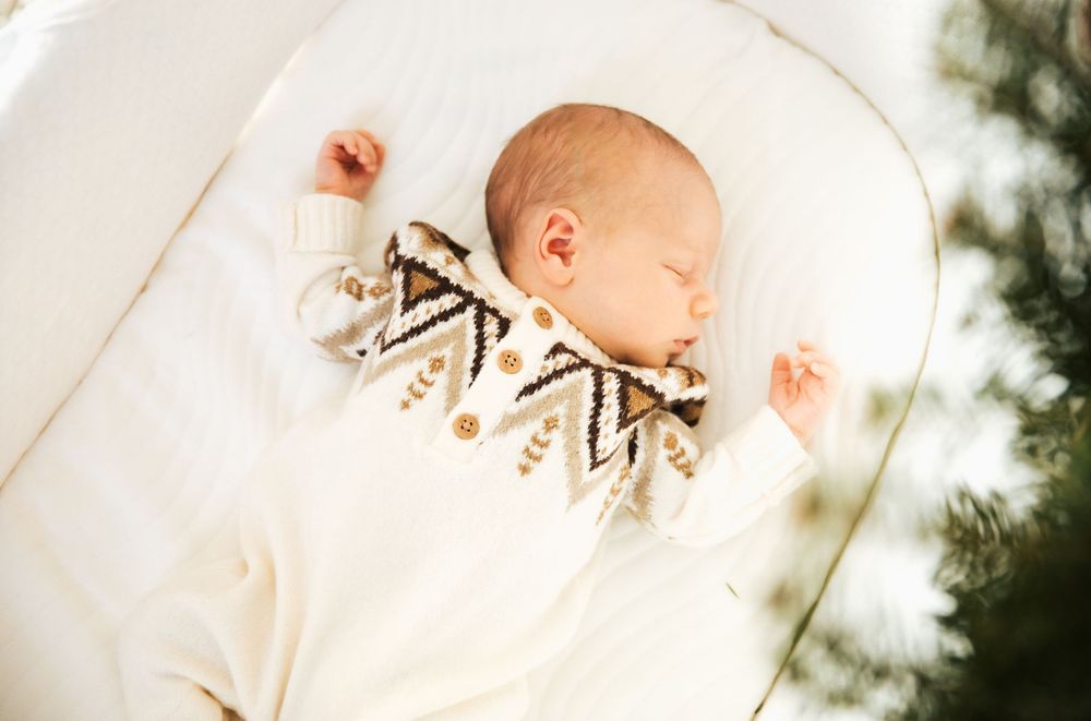 Newborn baby sleeping peacefully in a white bassinet wearing a cozy knit sweater with geometric patterns. Bristol Rhode Island Portsmouth