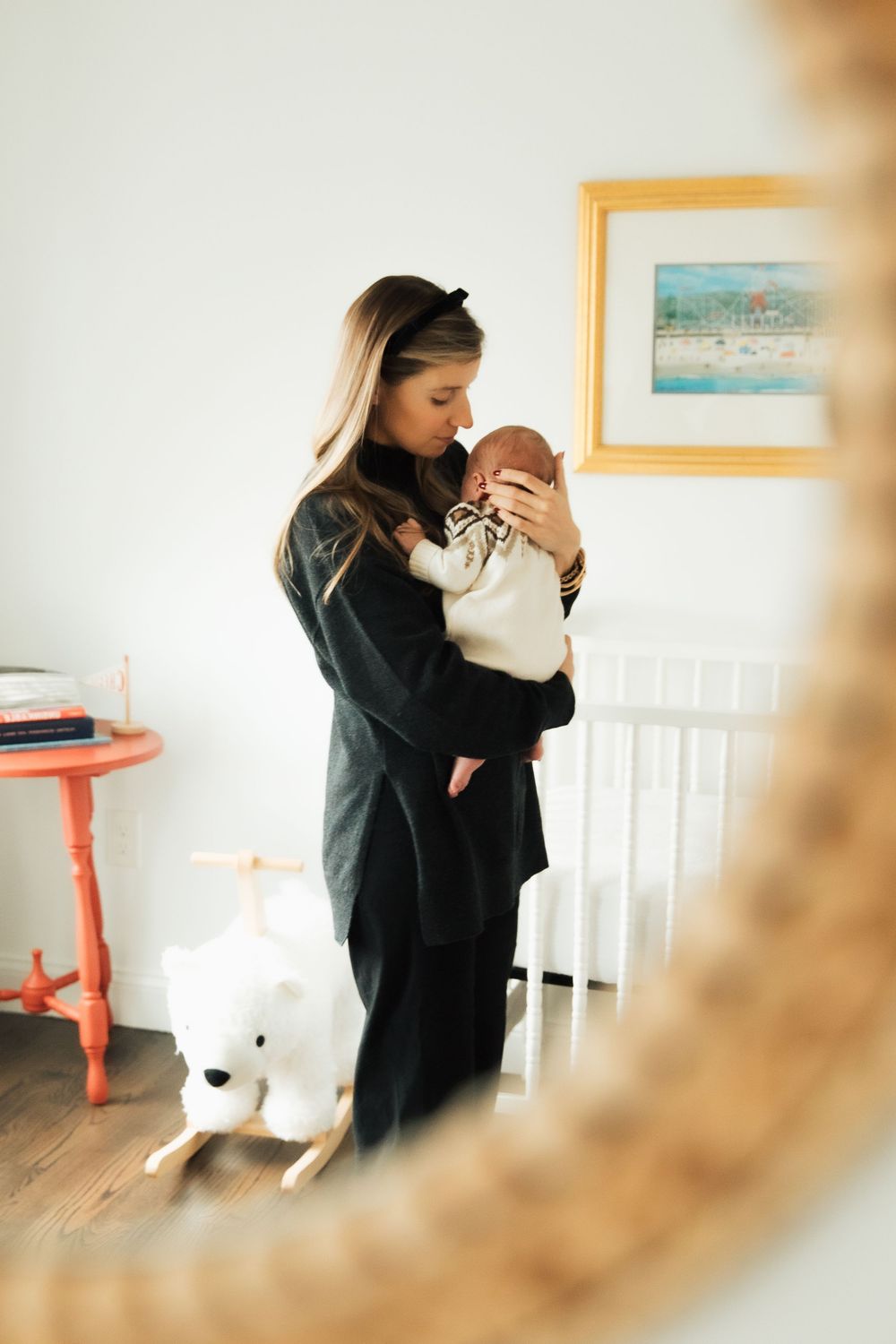 Mother in black dress tenderly holds newborn baby in bright nursery with white crib and rocking horse toy. Bristol Rhode Island Portsmouth