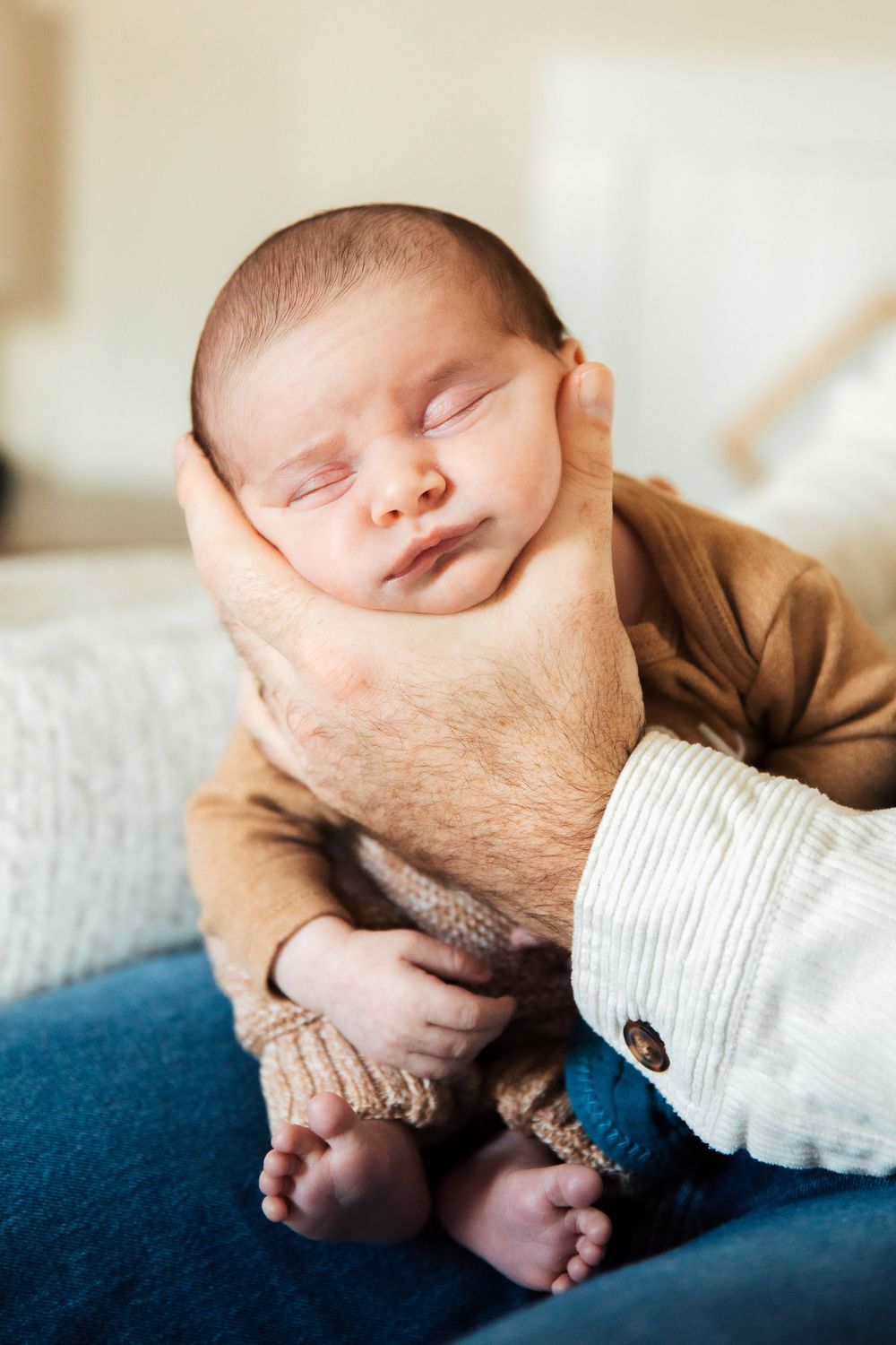 A newborn baby sleeping peacefully while being cradled in an adult's hands, wearing a cozy brown outfit. Bristol Rhode Island Portsmouth