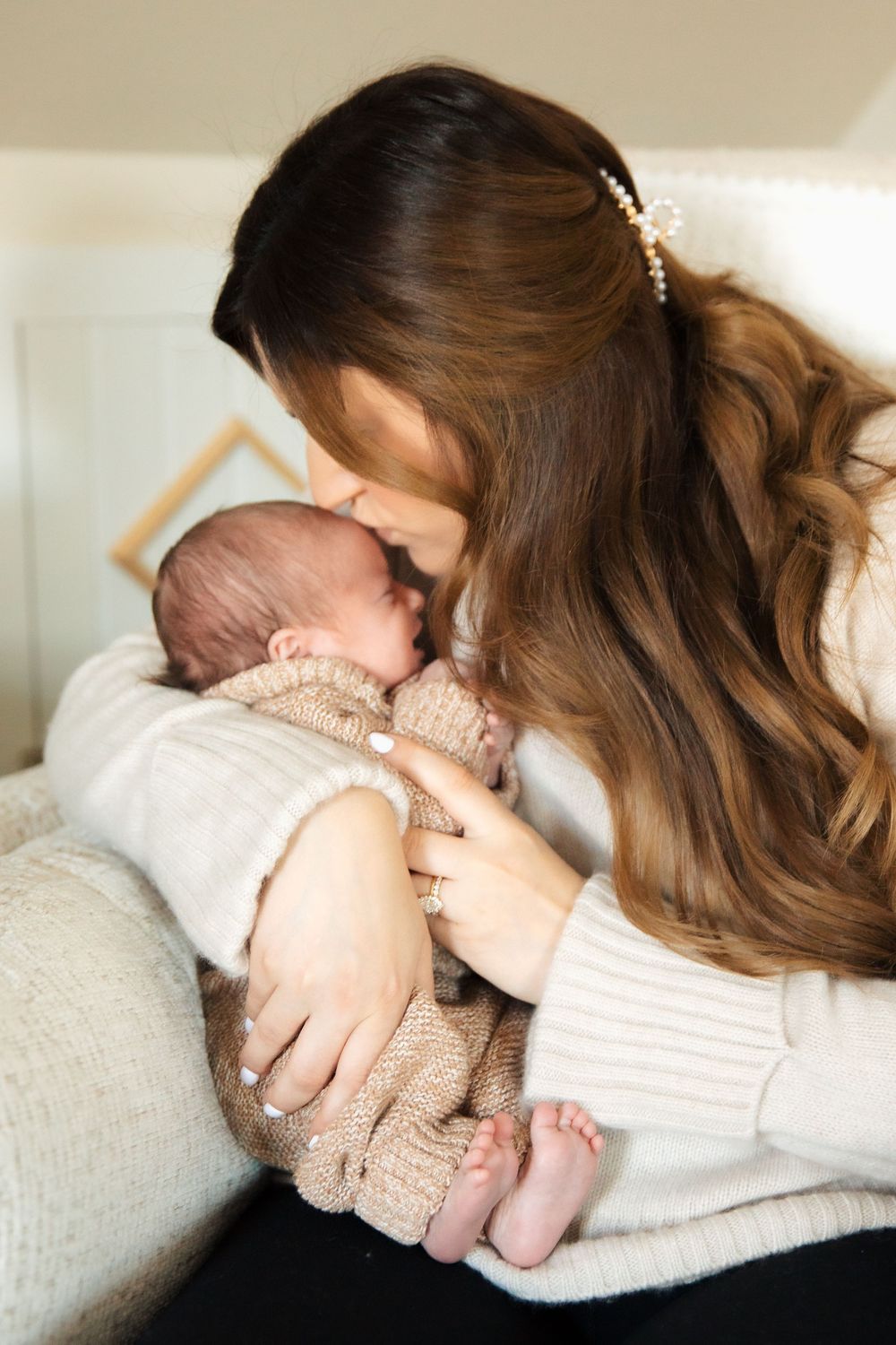 A mother with long brown hair gently kisses her newborn baby wrapped in a knit outfit. Bristol Rhode Island Portsmouth