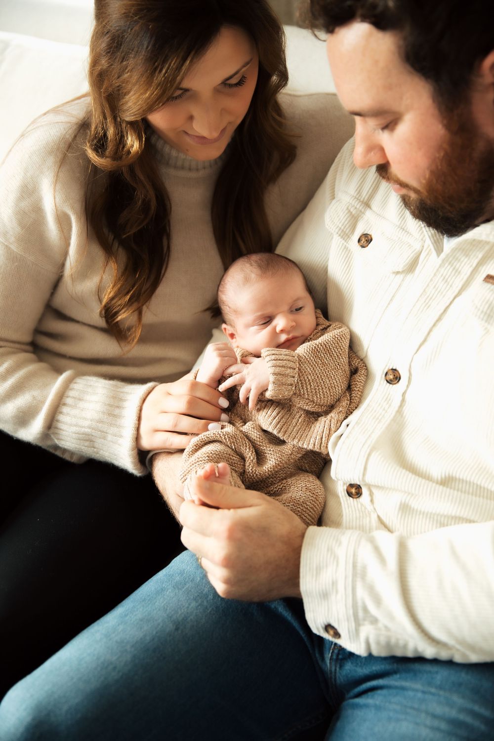 New parents lovingly cradling their sleeping newborn baby dressed in a cozy knit outfit. Bristol Rhode Island Portsmouth