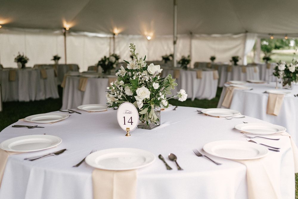 Elegant wedding reception table with white linens, floral centerpiece, and table number 14 under a tent.