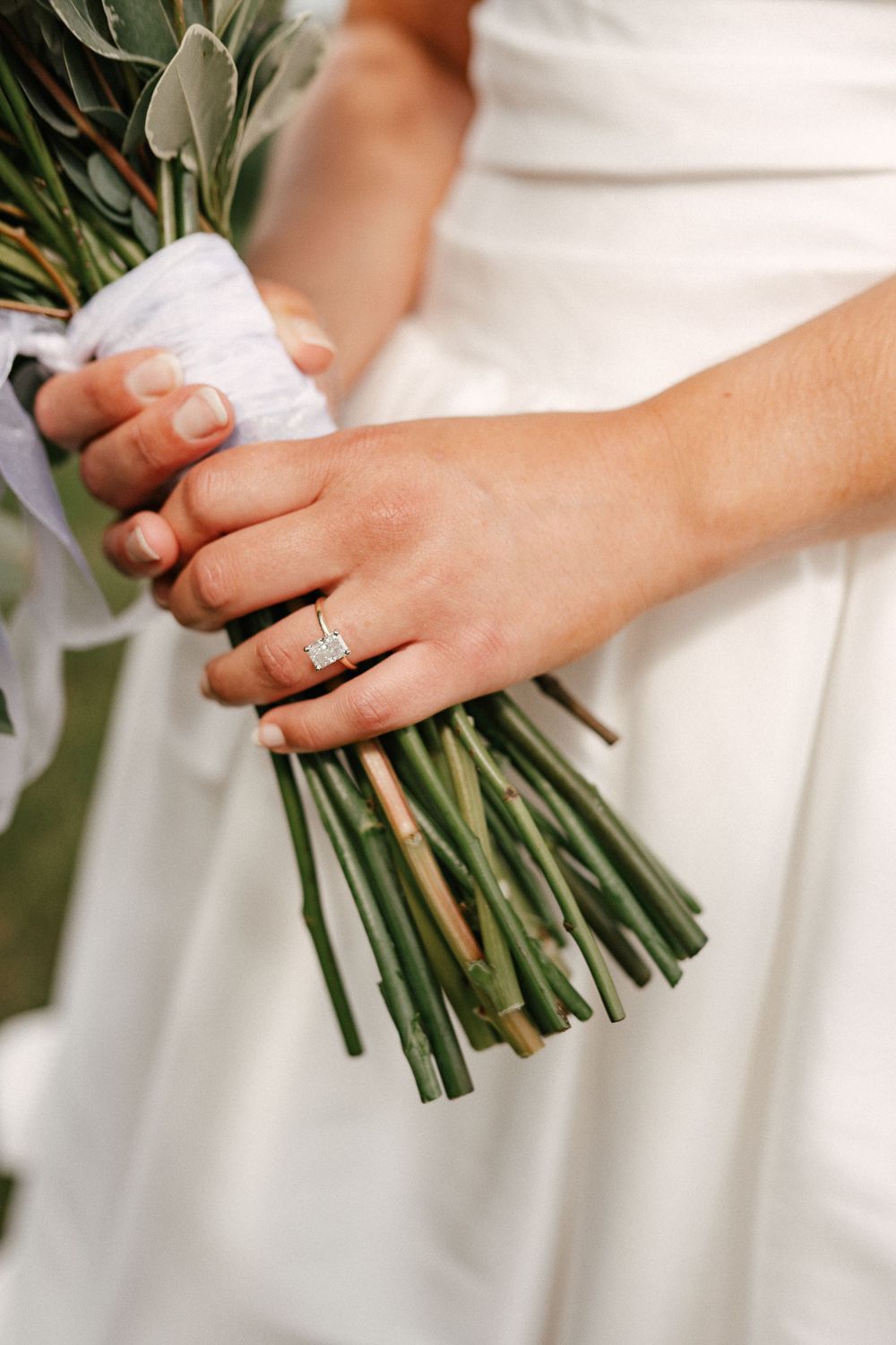 Bride holding a green stem bouquet with a elegant emerald-cut diamond engagement ring on her finger.