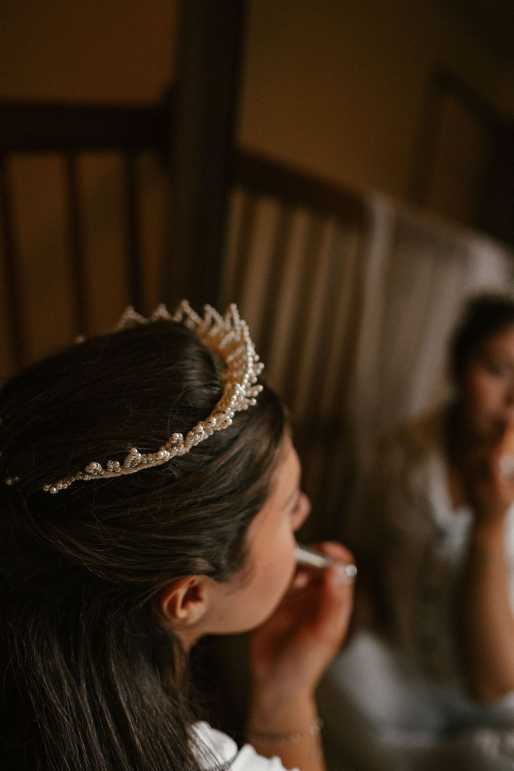 Bride wearing a sparkling tiara getting makeup applied while her reflection is visible in a mirror behind her.