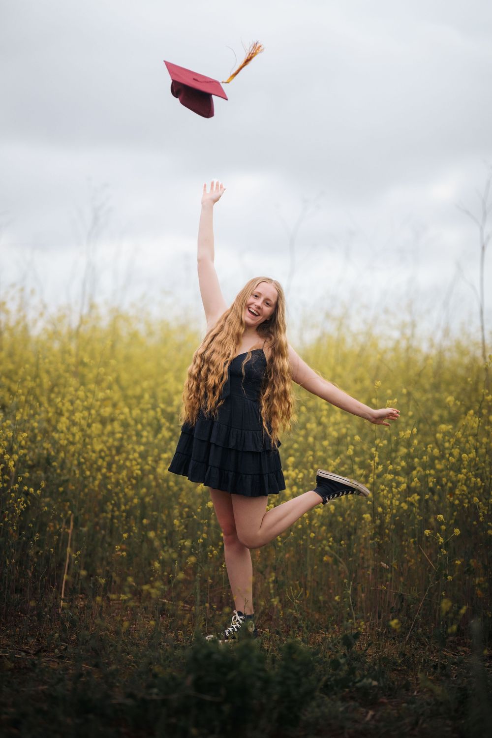 High school graduate Abbi poses in a maroon cap and black dress among wildflowers, captured by Chris Cornish Photography.