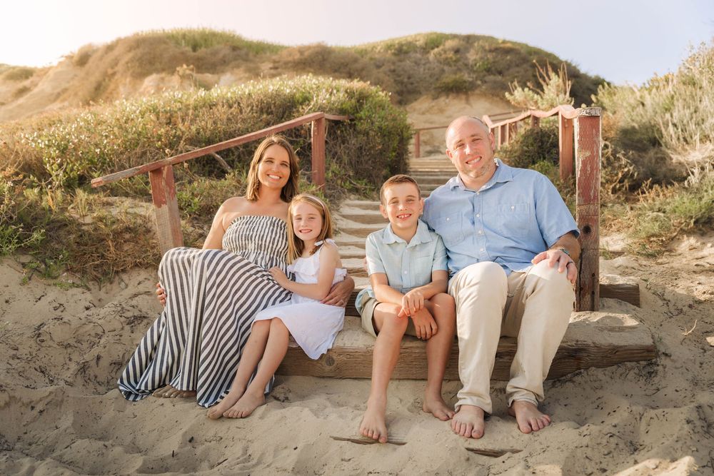 Family of four smiles and poses together on the beach with ocean waves behind them at Crystal Cove, captured by Chris Cornish Photography.