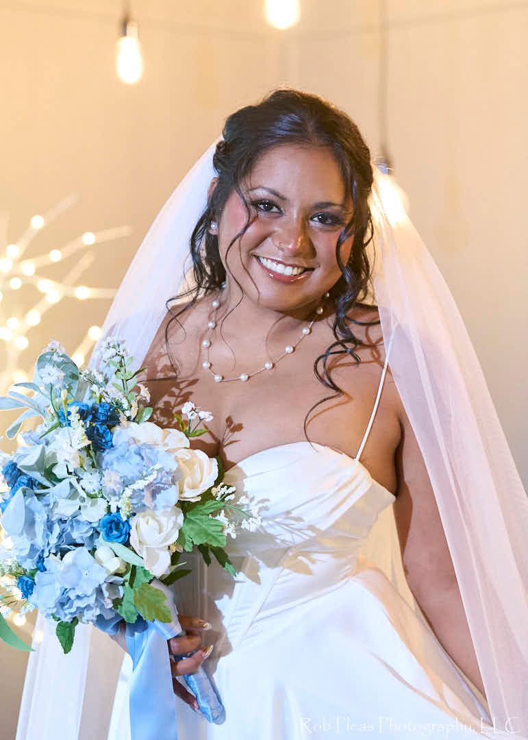 Formal of bride on church stage.  She is holding her dress with one hand and a beautiful blue bouquet with the other.