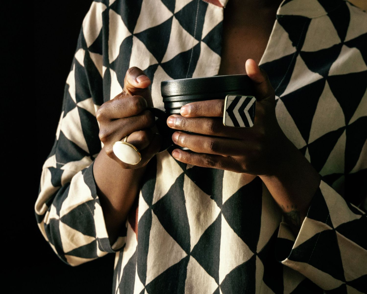 Hands holding cup against geometric black and white patterned background.