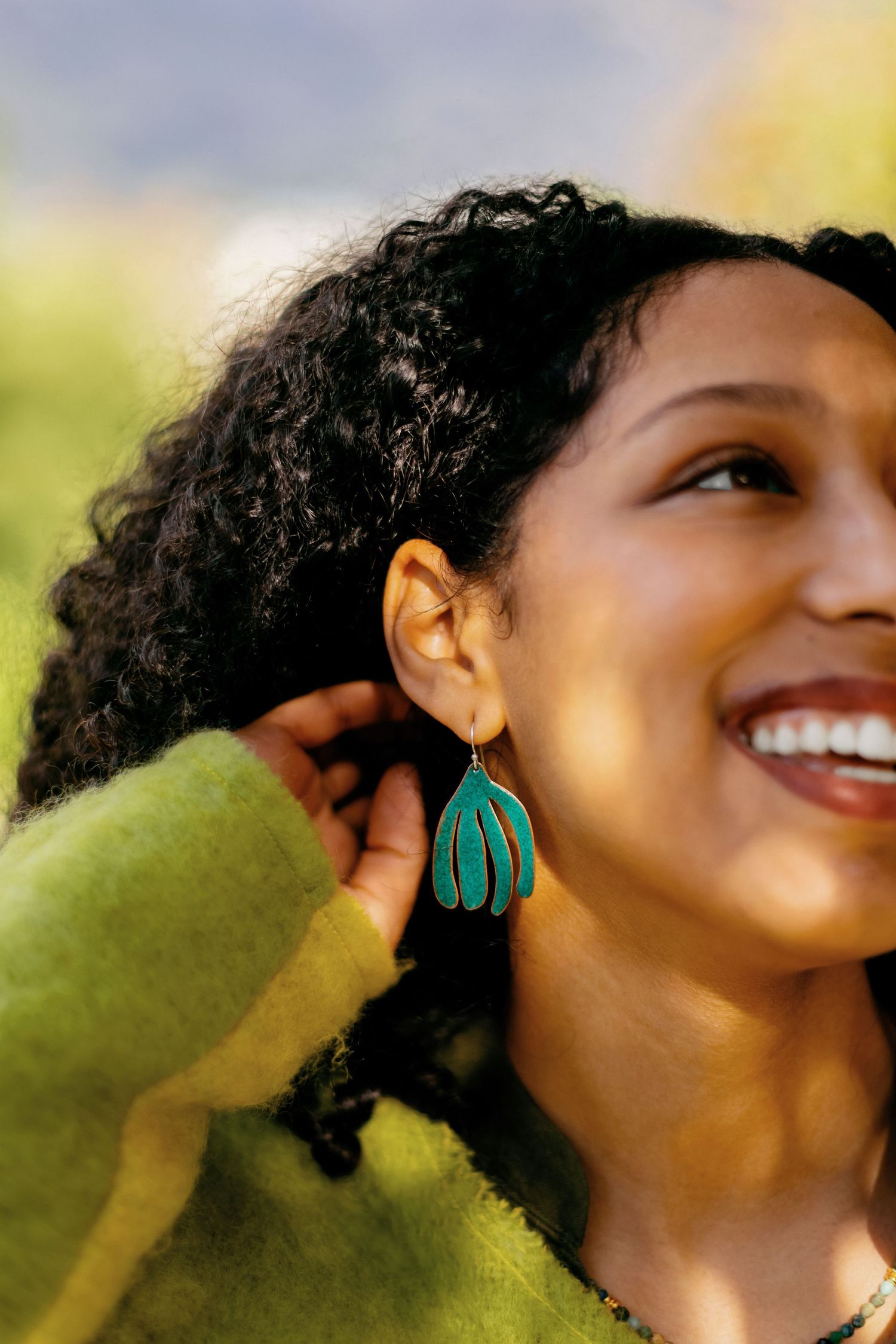 Profile view of person wearing turquoise earrings against blurred natural background.