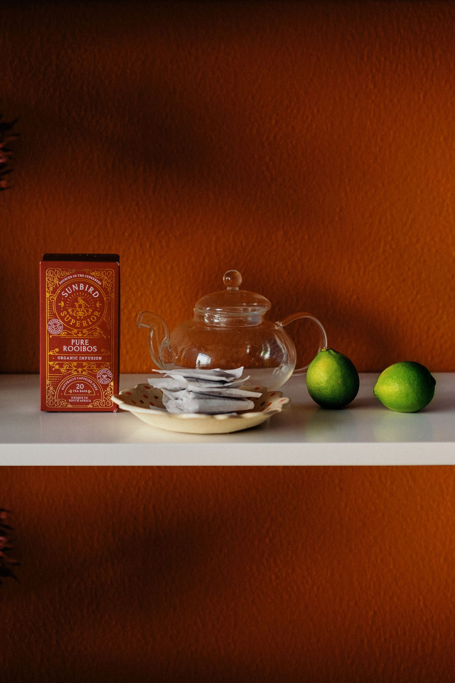 Still life composition with glass dishes, limes and vintage boxes on white shelf.